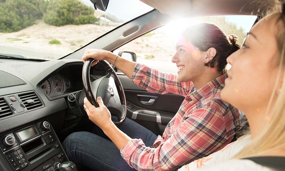 Young man driving his car with a female friend during the day